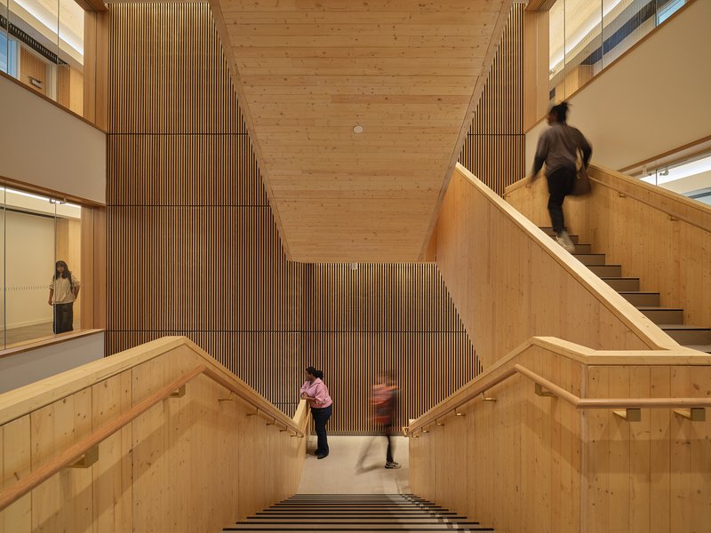 View down the timber-clad stairwell with vertical slatted wall as people ascend and descend