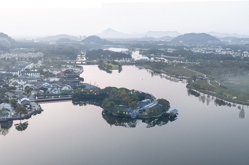 Wide aerial view of the island pavilion within the lake and surrounding village in morning mist