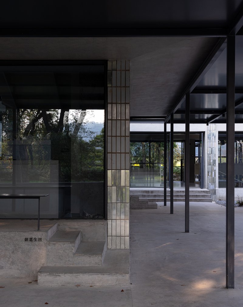 Covered walkway with steel columns and deep overhang framing views of trees and a distant water body