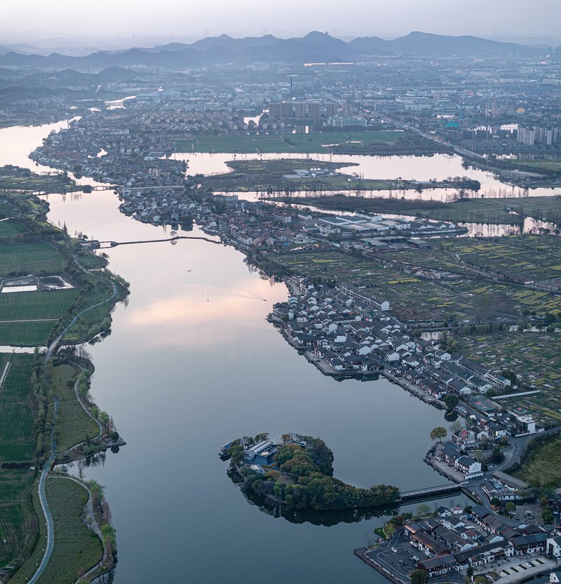 Aerial view of lake with small wooded island and surrounding agricultural fields and settlements at twilight