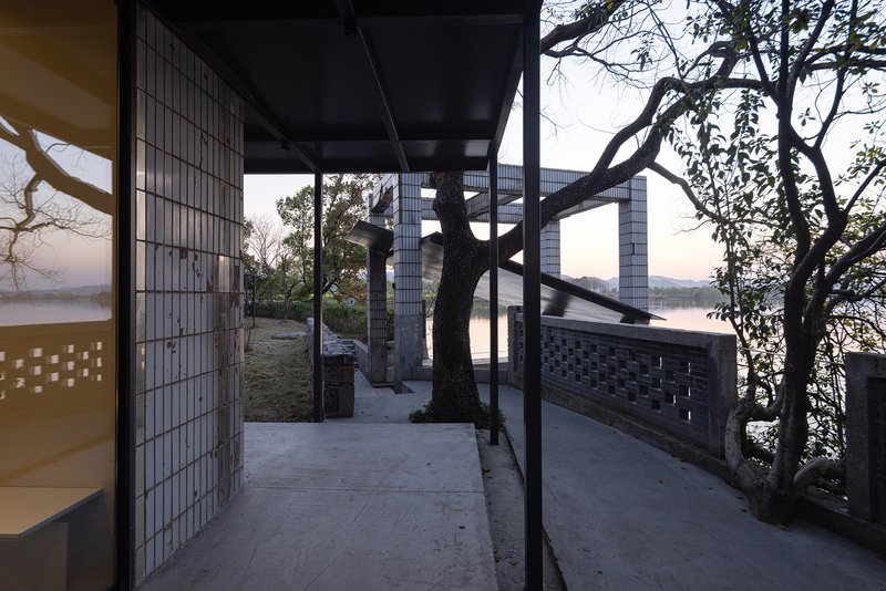 Exterior terrace framed by steel columns and glass block walls with preserved trees at dusk