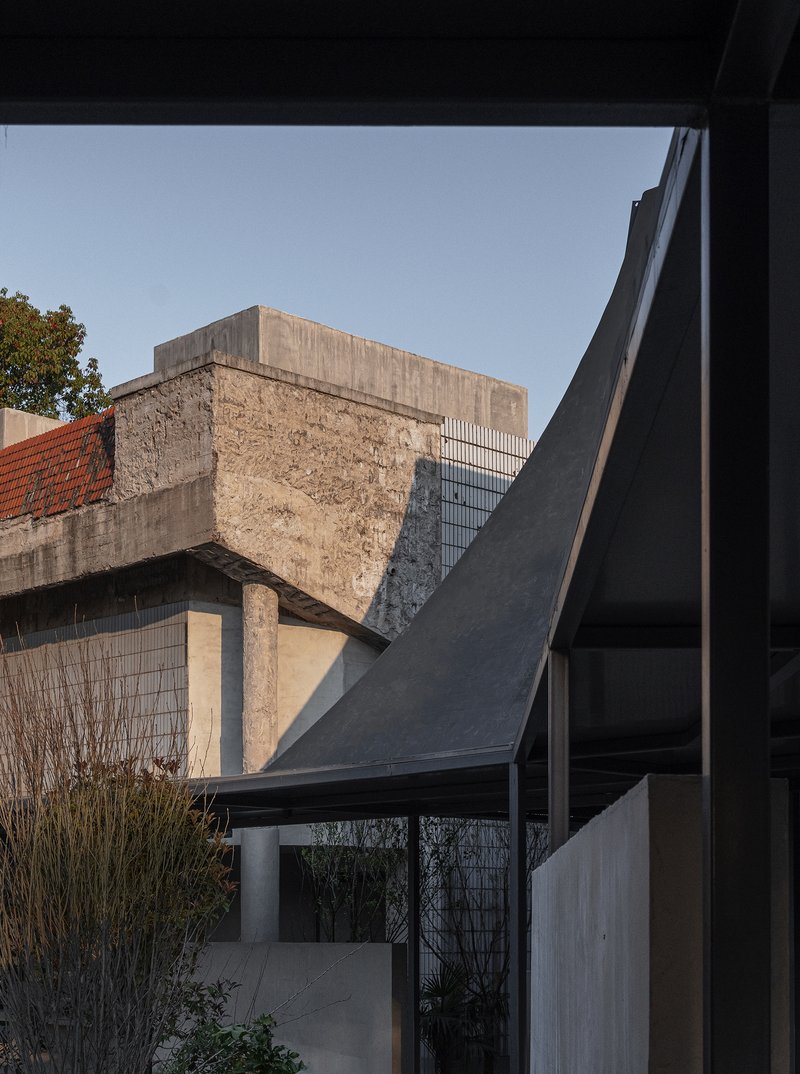 Framed view of exposed concrete bridge remnant and angular roof forms from within the pavilion