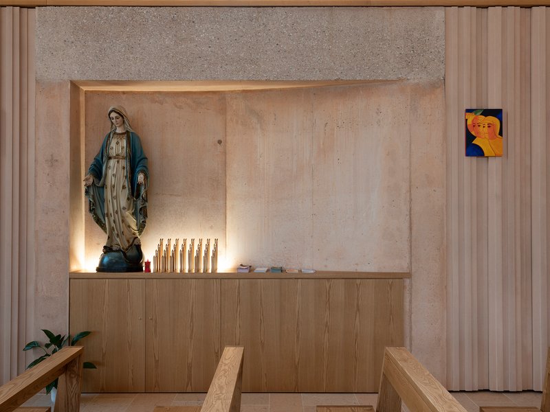 Niche in concrete wall with religious statue, candles and timber cabinetry below