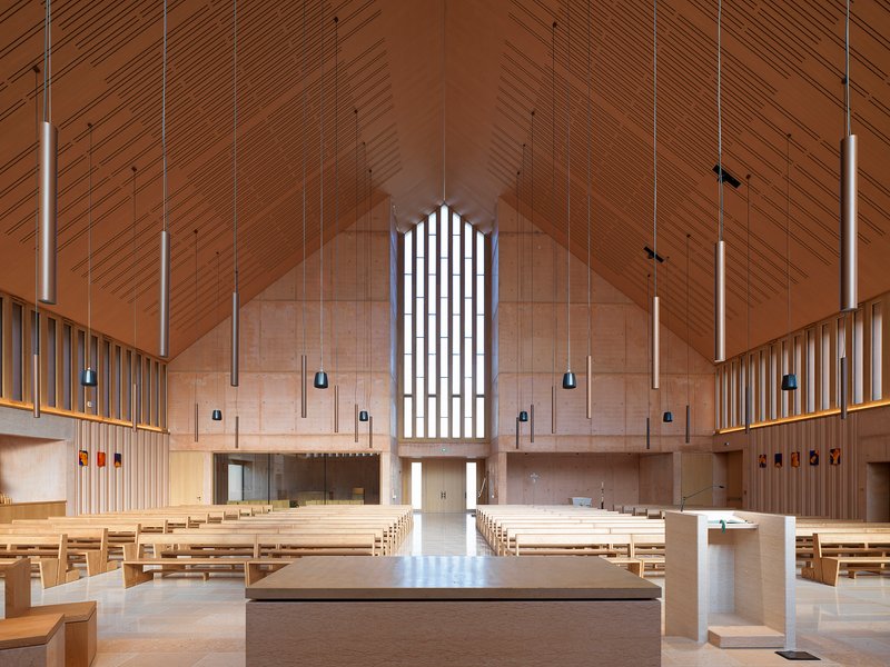 Interior sanctuary with timber-clad pitched ceiling, pendant lights and an arched window above the altar