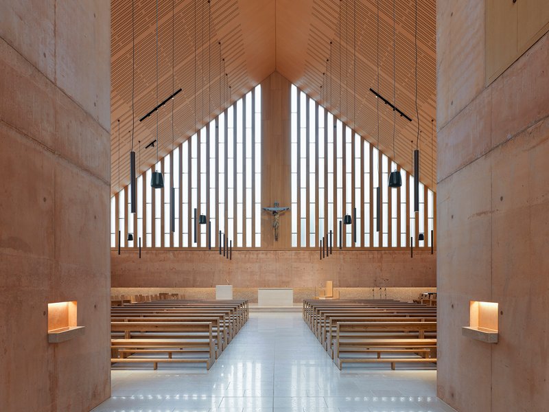 Sanctuary interior with wooden pews facing a vertical slatted window wall and timber ceiling panels