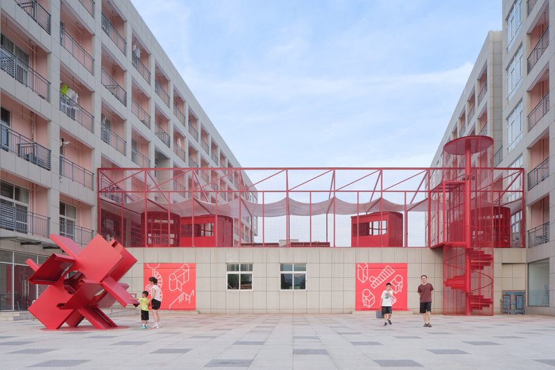 Red steel frame pavilions with translucent walls sheltering a courtyard entry with children playing beneath