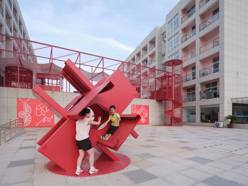 Tilted red sculpture with circular opening provides a climbing structure for children in the courtyard