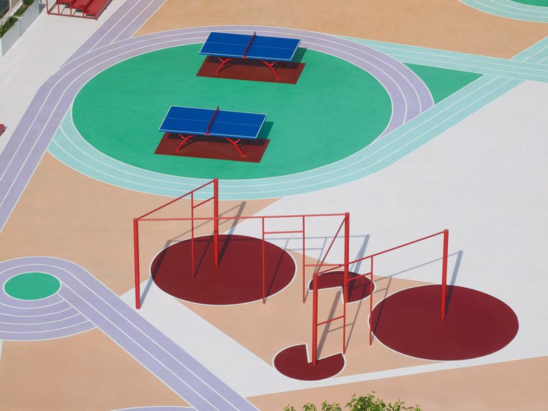 Overhead view of red steel play equipment with circular platforms and table tennis tables on circular turf patches