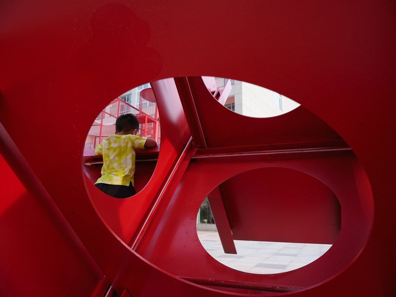 Interior view through circular cutouts in red metal partition with child climbing above