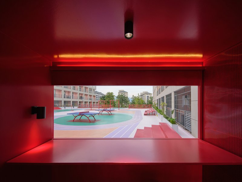 View through red metal roller shutter opening to courtyard with perforated ceiling above