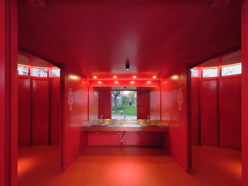 Red washroom with central basin counter and clerestory windows framing view to green courtyard beyond