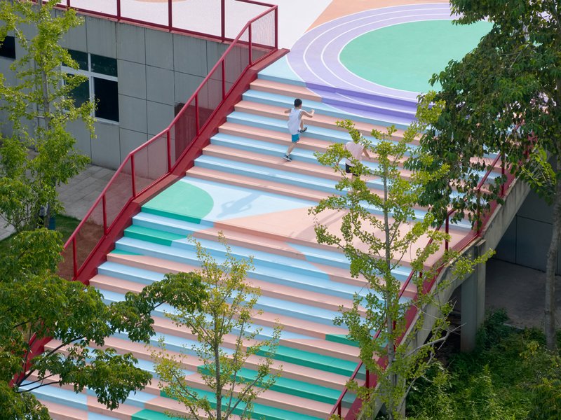 Striped pastel staircase with child running upward framed by trees and red steel railings