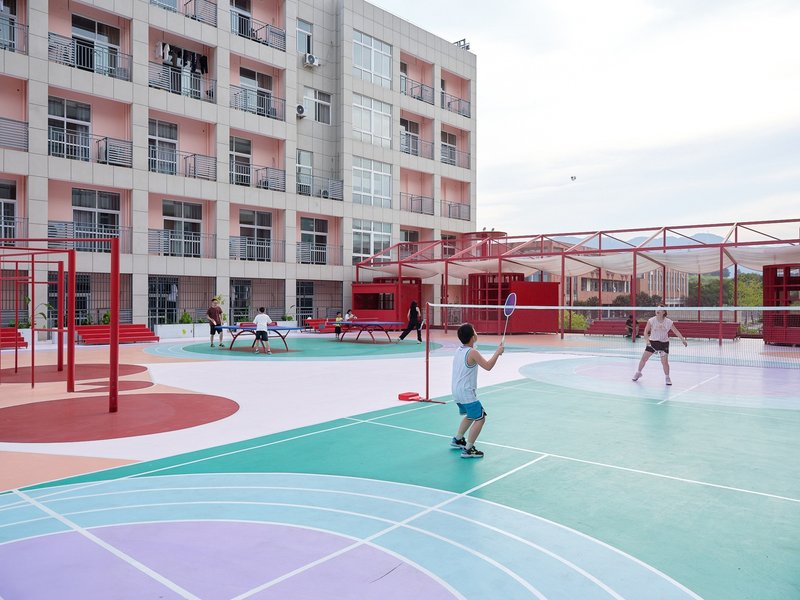 Multicolored court surface with children playing badminton beneath red steel frame structures
