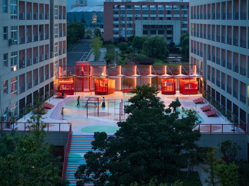 Aerial view of illuminated red pavilion with sawtooth roof on rooftop courtyard at dusk