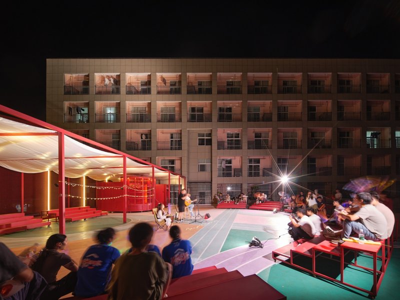 Night view of audience watching outdoor performance on rooftop court with lit red pavilion