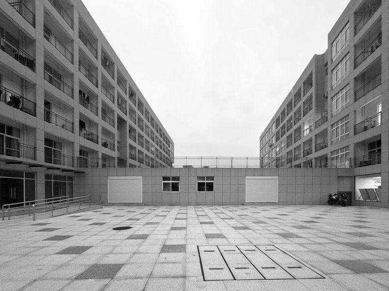 Central courtyard with patterned stone pavers flanked by repetitive concrete residential blocks under overcast skies