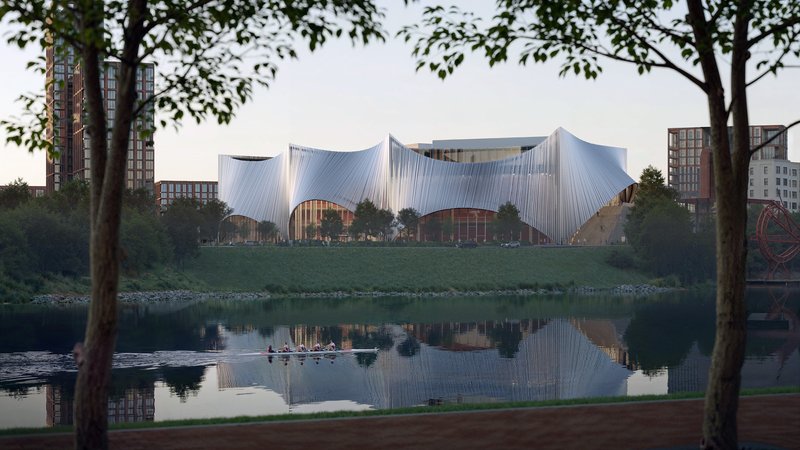 Undulating metallic roof form reflected in a calm waterway, viewed through trees at dusk