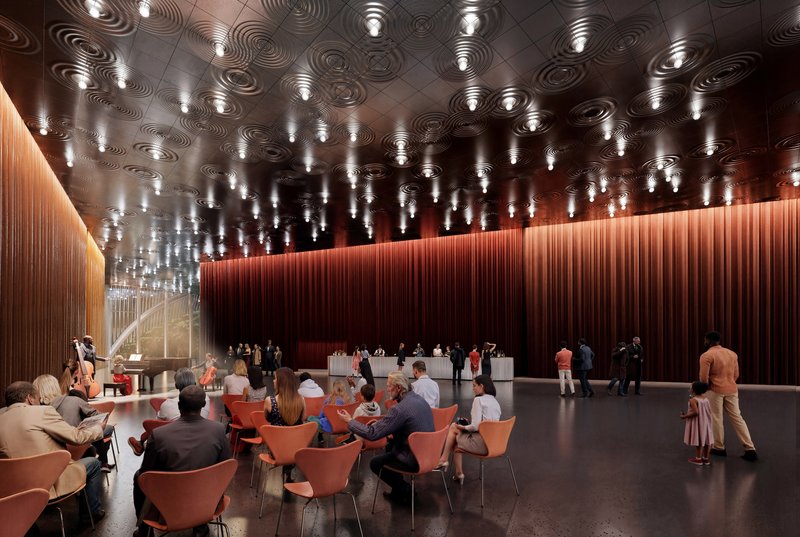 Performance hall foyer with sculptural ceiling panels, pendant lights, and visitors gathered around coral-colored seating