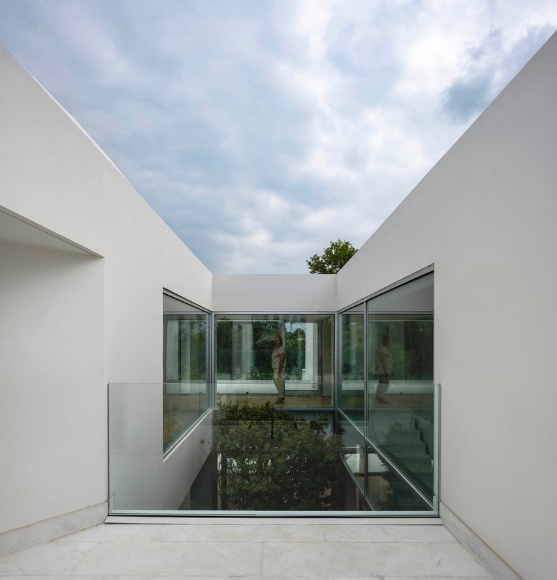 Glass-floored bridge spanning the sunken courtyard between white rendered walls open to the sky