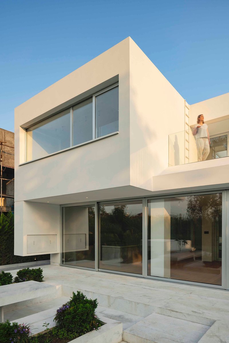 White rendered facade with full-height glazing and upper-level balcony at dusk with a figure visible