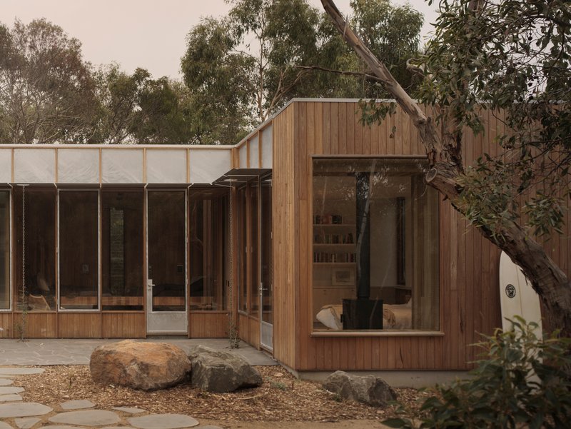Timber-clad volumes with glazed openings and translucent upper panels arranged around a garden courtyard with boulders