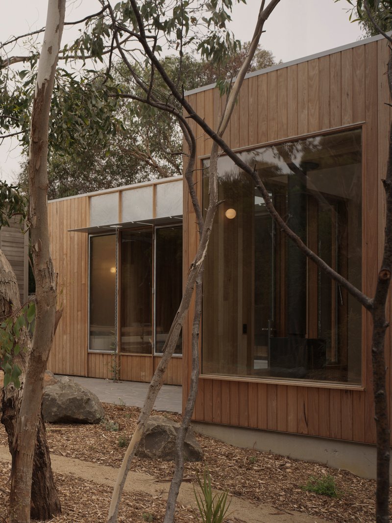 Vertical timber cladding and glazed facades framed by mature trees in an overcast garden setting