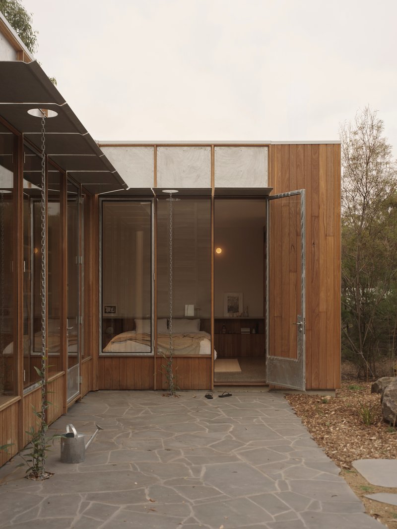 Covered exterior terrace with hanging swing seat and stone paving looking into a bedroom volume at dusk