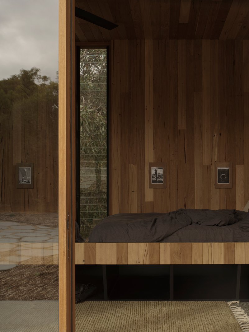 Interior bedroom with vertical timber wall cladding and built-in platform bed beside a glass door