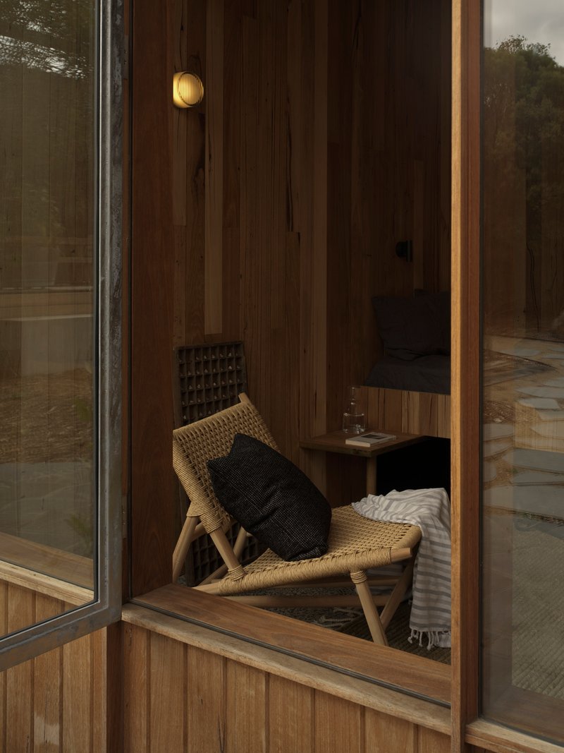 Woven chair against timber-paneled wall visible through glazed sliding door from exterior courtyard