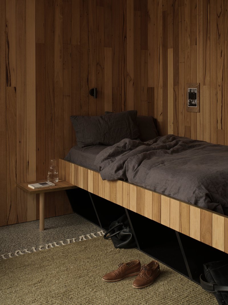 Sleeping area with platform bed and storage underneath on textured carpet beside timber side table