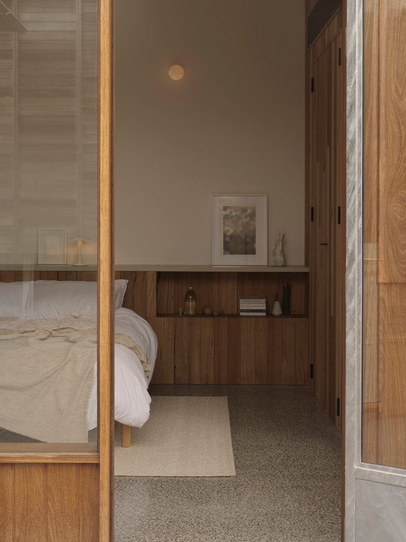Bedroom alcove with built-in timber cabinetry and terrazzo flooring visible through glass partition