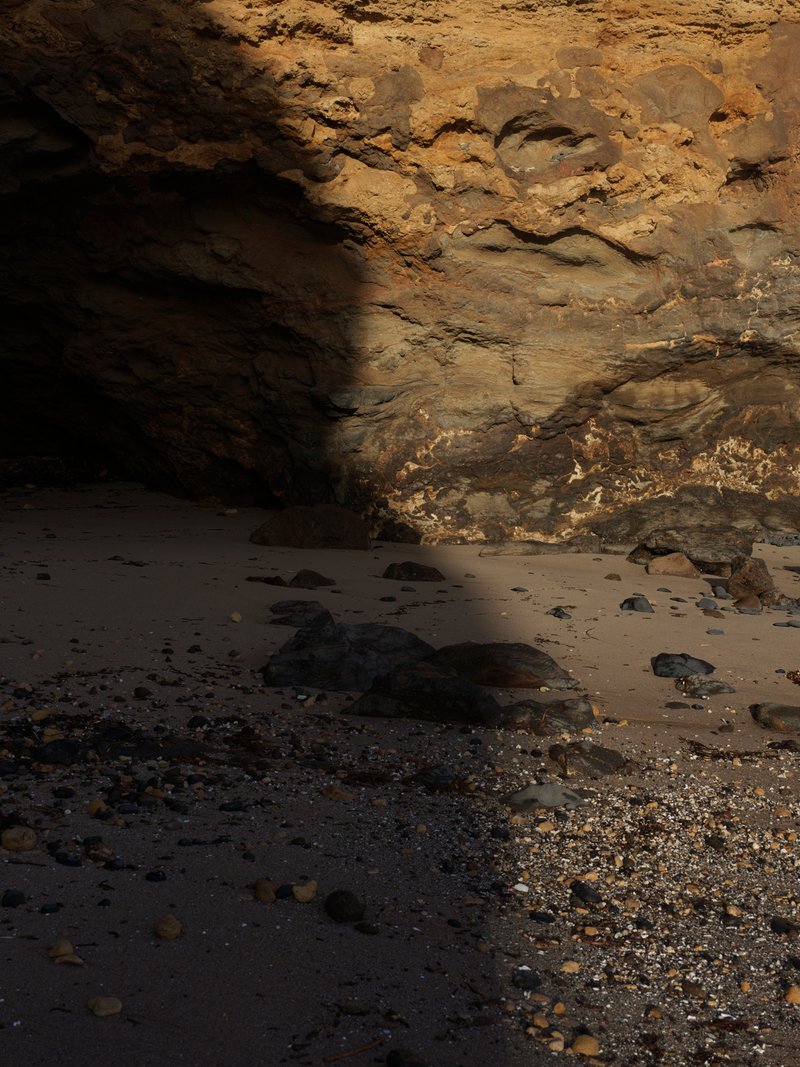 Natural sandstone overhang with layered sediment formations above a pebbled floor in shadow
