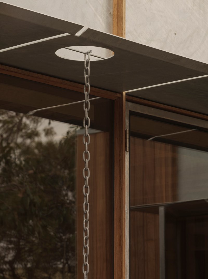 Rain chain suspended from timber-framed eave with concrete soffit overlooking vegetation
