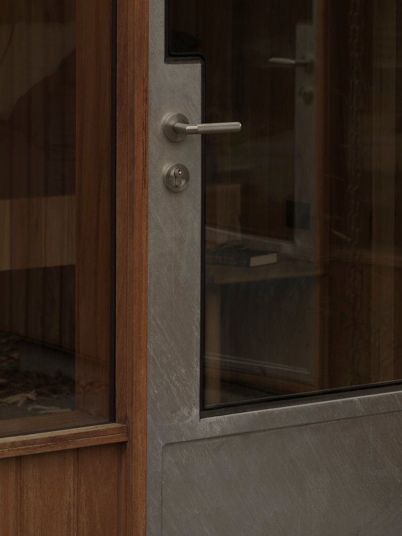 Timber and glass door with brushed metal lever handle and concrete frame edge