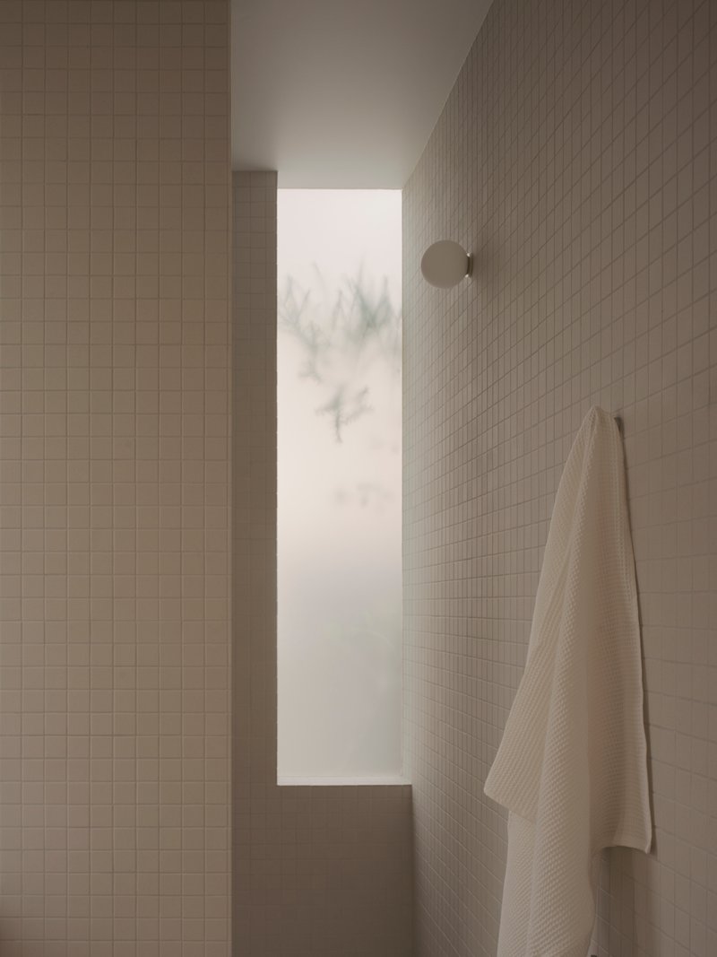 Tiled bathroom corner with narrow window framing winter trees in mist