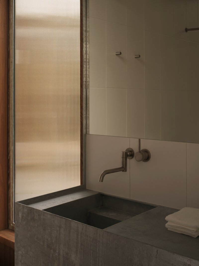 Concrete vanity basin with wall-mounted tap beside a fluted glass window filtering daylight