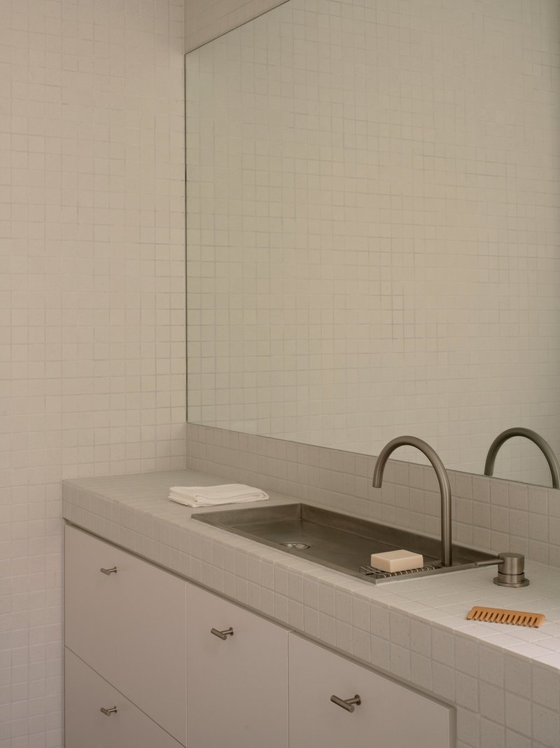 White tiled bathroom vanity with dual basins and integrated concrete countertop beneath a frameless mirror