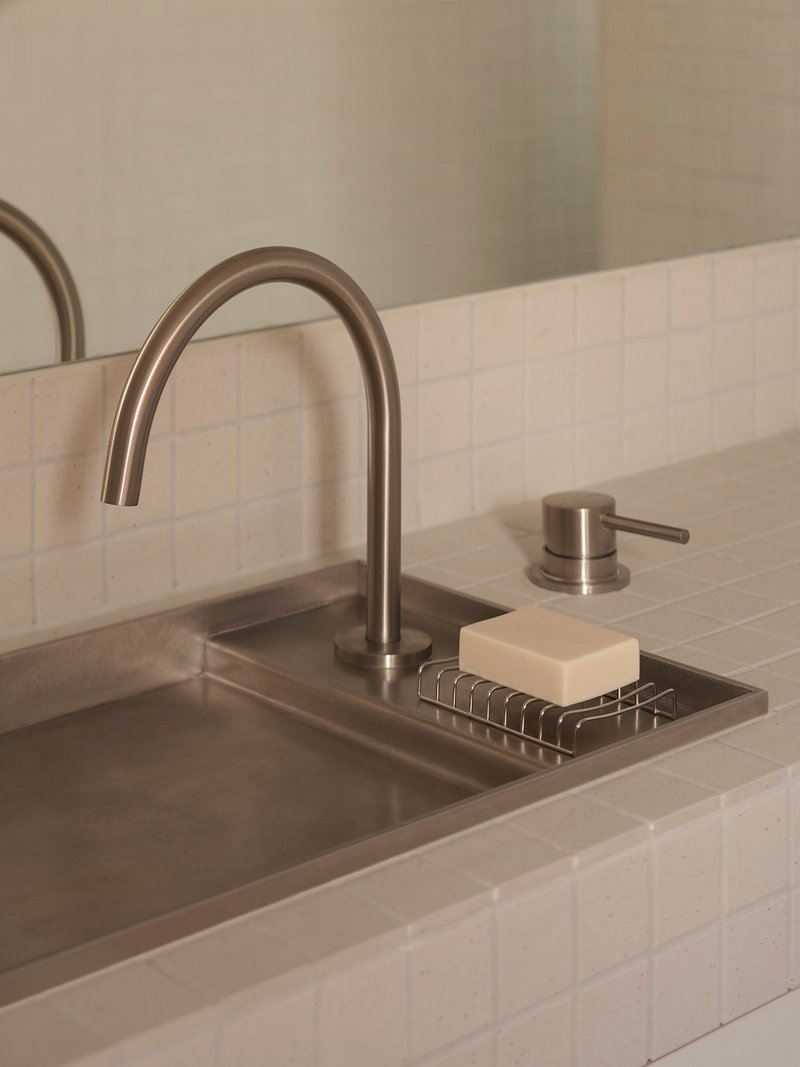 Close-up of brushed steel faucet and soap dish inset in concrete bathroom basin