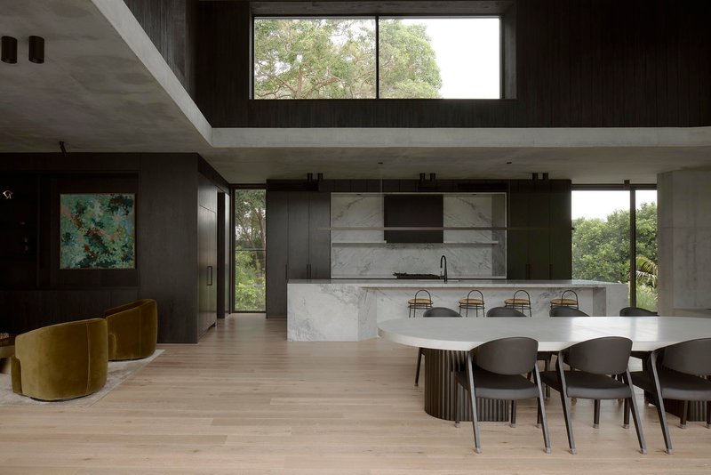 Double-height living space with marble island, dining table and clerestory window overlooking trees