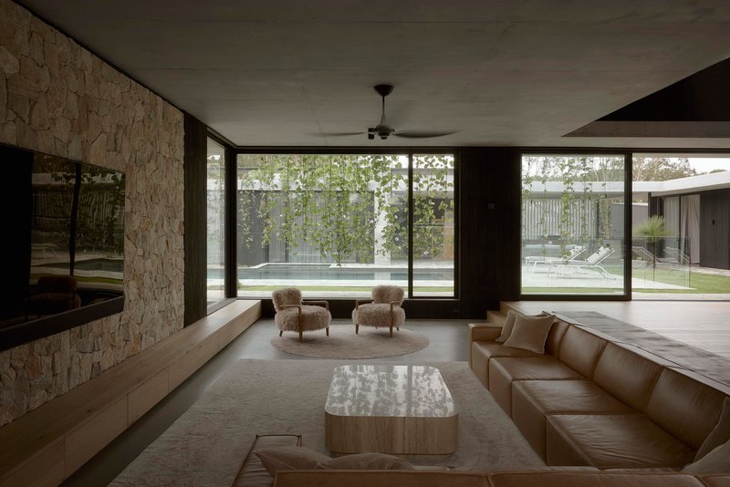 Sunken lounge with textured stone wall and floor-to-ceiling glazing opening to pool courtyard