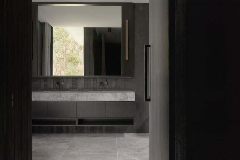 Bathroom vanity with marble countertop, dark tile and mirror reflecting trees outside