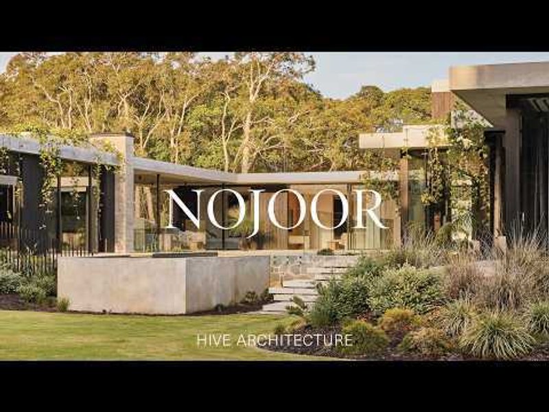 Concrete entrance wall with metal lettering amid landscaped garden beds in afternoon light