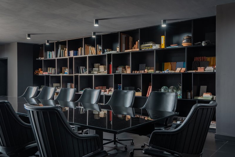 Conference room with a black table, upholstered chairs, and floor-to-ceiling bookshelf in artificial light