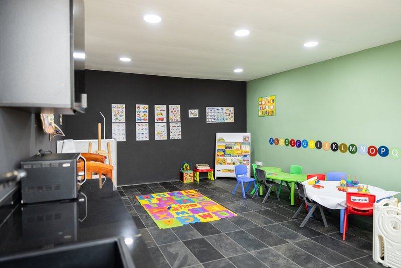 Children's playroom with pale green and charcoal walls, alphabet letters, and colorful furniture on tile flooring