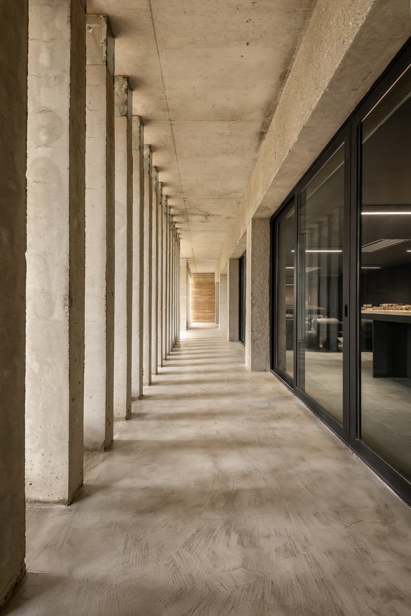 Interior corridor with rhythmic concrete columns and herringbone floor pattern alongside glazed offices
