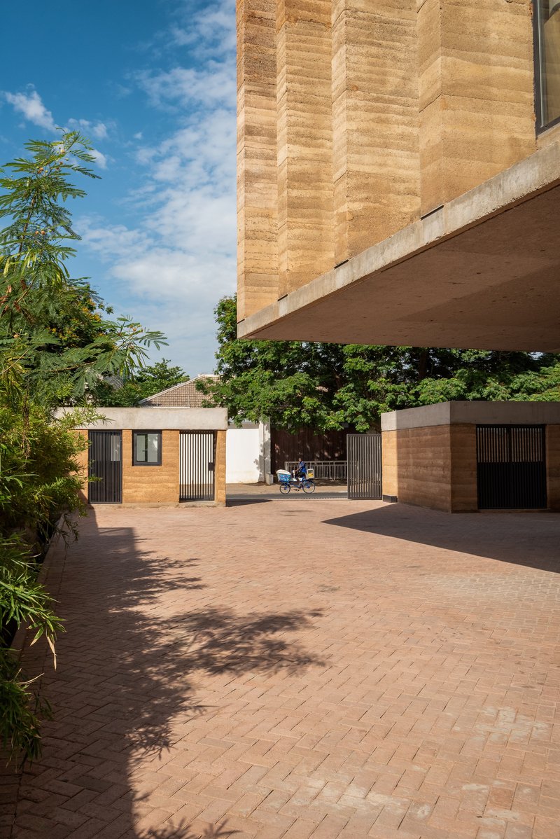 Paved courtyard beneath the cantilevered upper floor with motorcycle and tree shadows across terracotta pavers