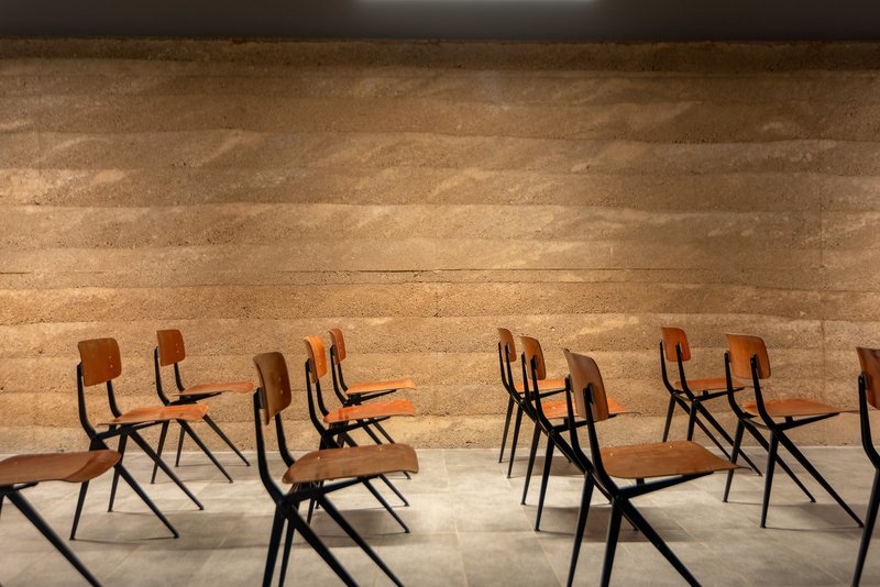 Row of wooden school chairs arranged before a horizontal layered rammed earth wall