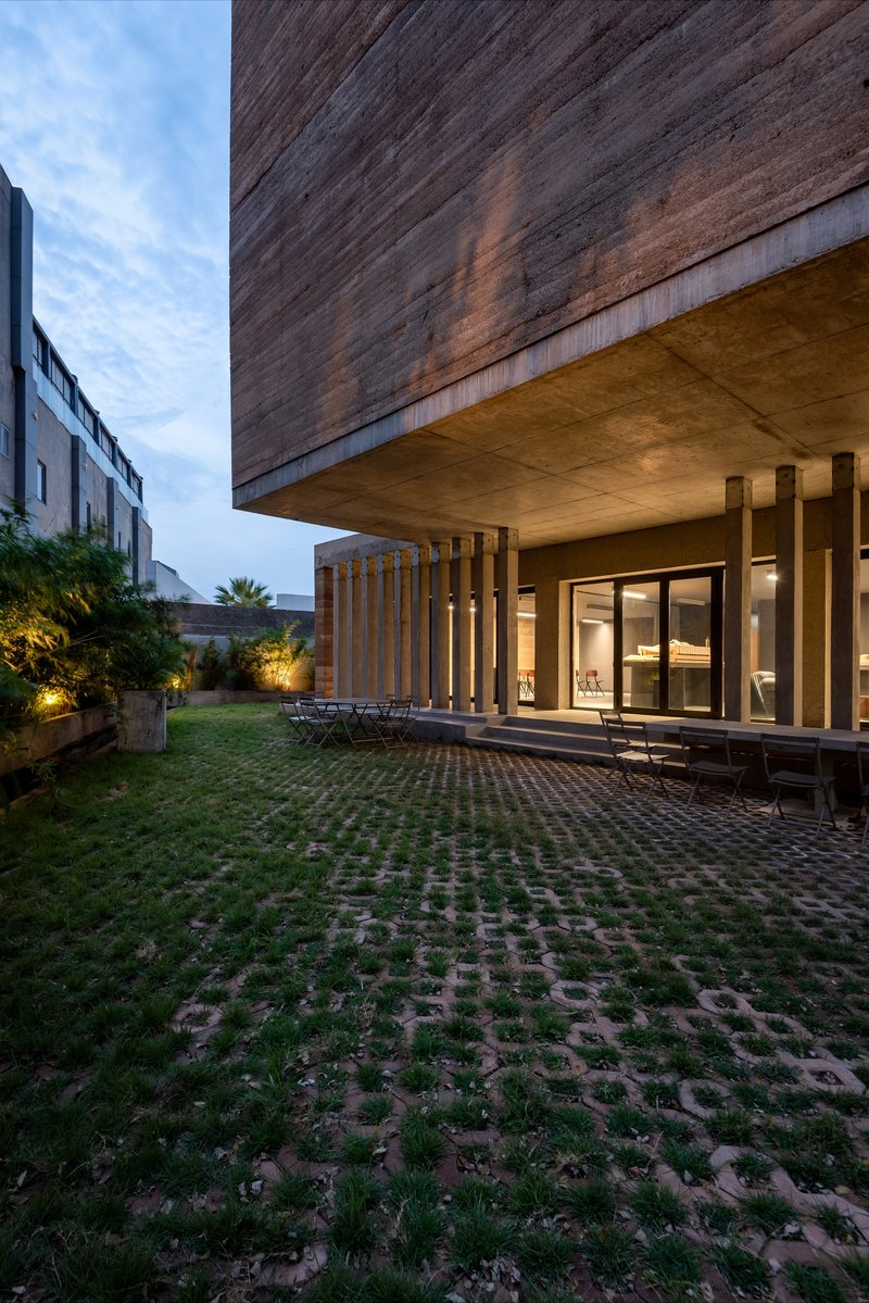 Courtyard view of the cantilevered timber-clad volume above a colonnade at dusk
