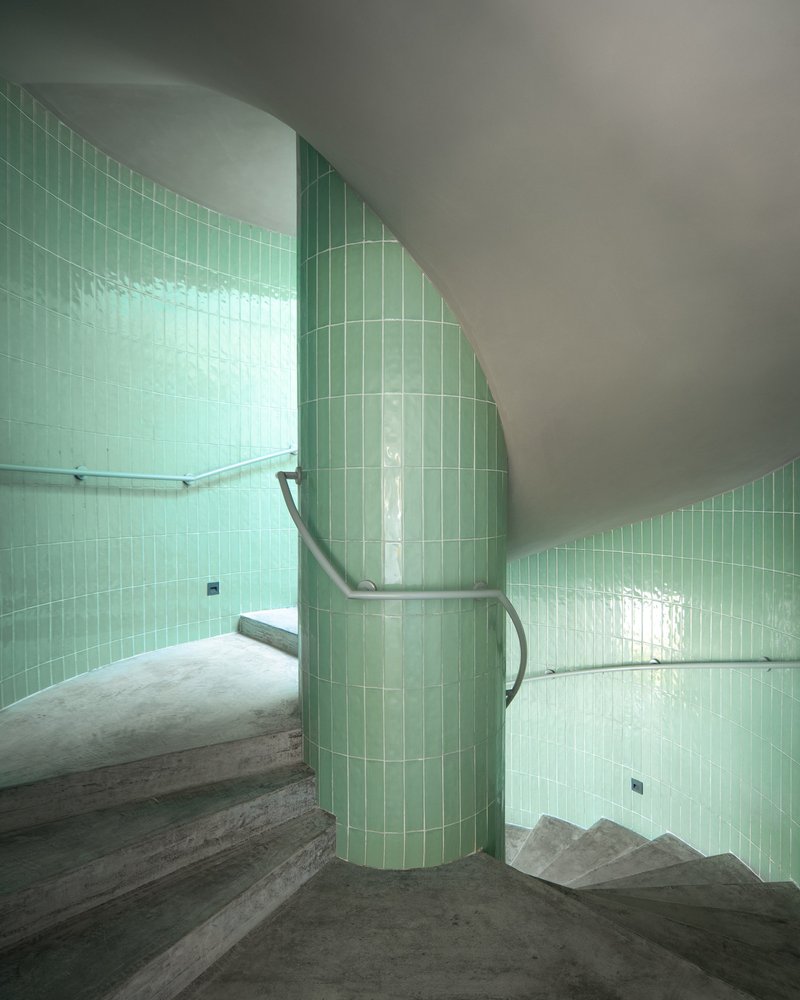 Curved stairwell wrapped in pale green subway tile with concrete treads and metal handrail