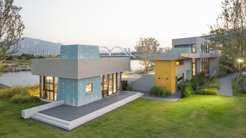 Elevated view of the waterside complex with green glass block volume and yellow entrance pavilion at dusk